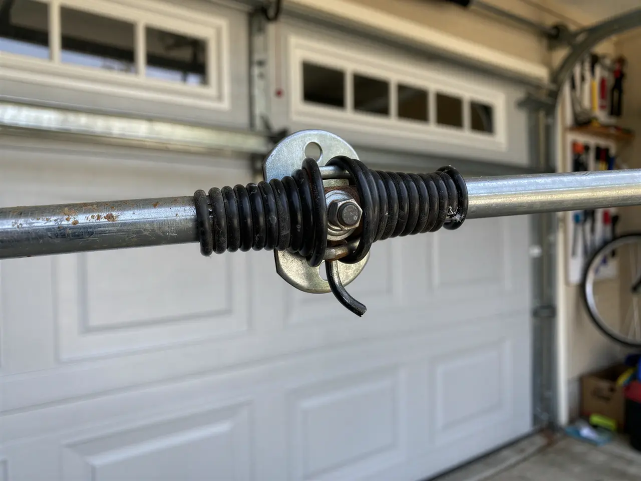 A broken torsion spring is wrapped around a metal rod above a white garage door.